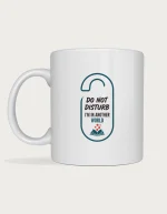 Funny reading mug with a door hanger sign design reading Do Not Disturb, I'm In Another World with a small open book, on a white ceramic mug