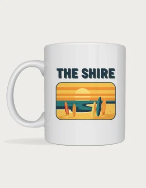 The shire mug: Retro postcard with the words The Shire above a surf beach at sunset with surfboards standing in the sand